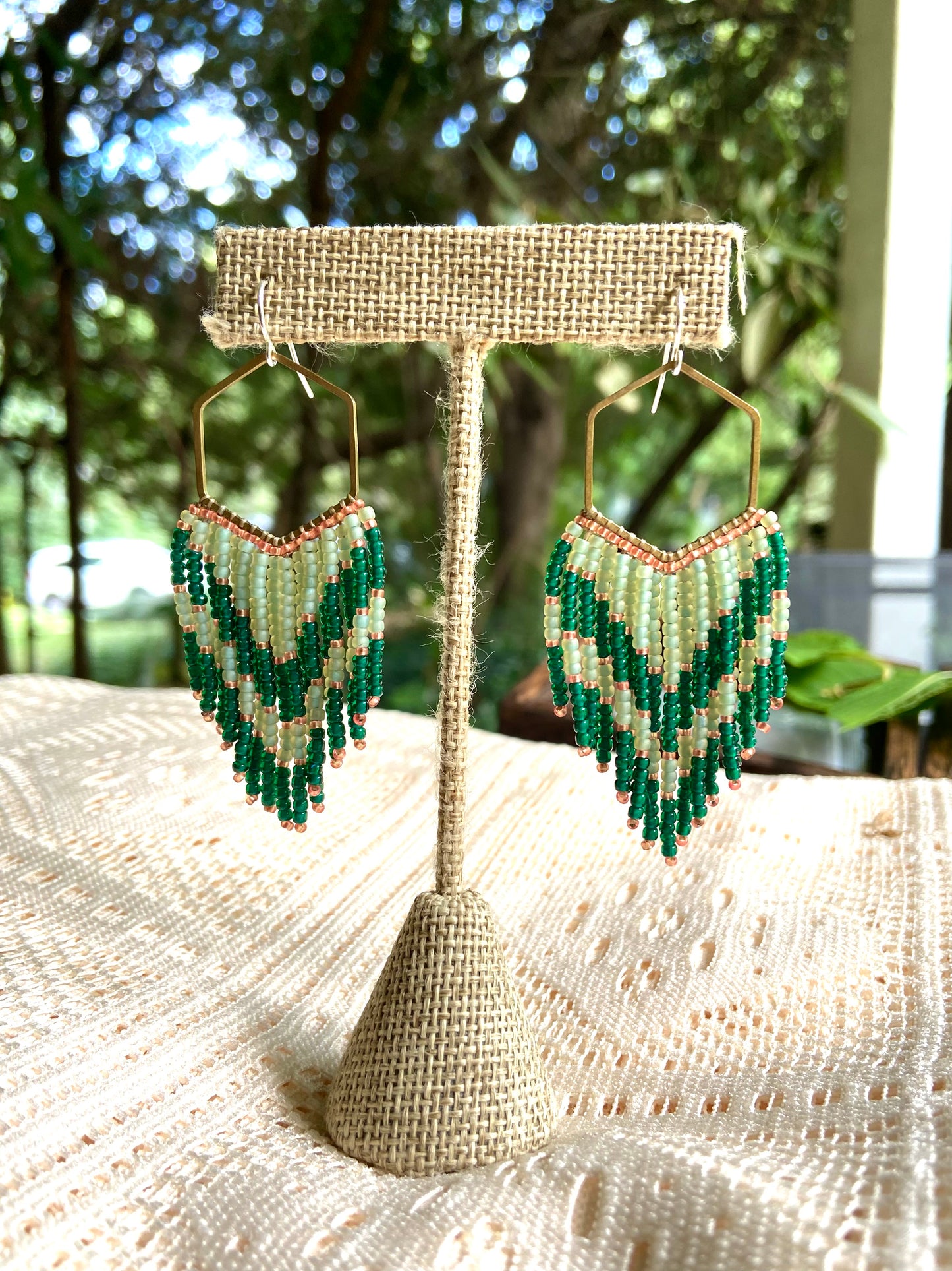 Green beaded earrings on a decorative stand with a natural background