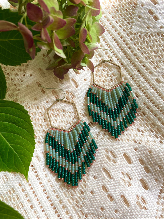 Green beaded earrings on a textured white surface with green leaves.