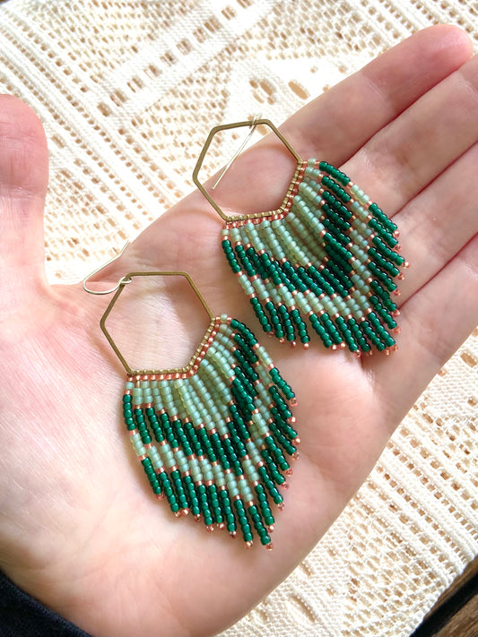 Green beaded earrings held in a hand against a textured background