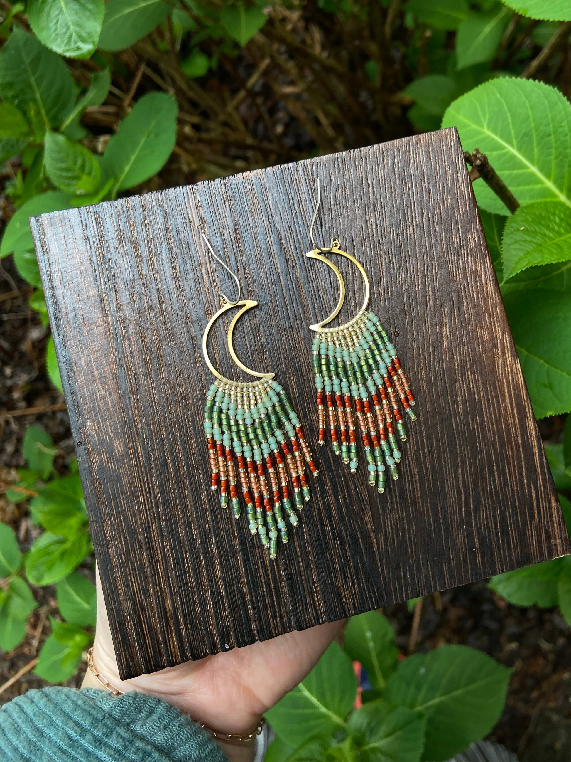 Beaded earrings displayed on a wooden box with green leaves in the background
