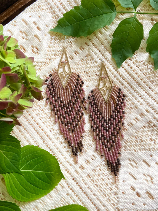 Beaded earrings on a textured fabric background with green leaves.