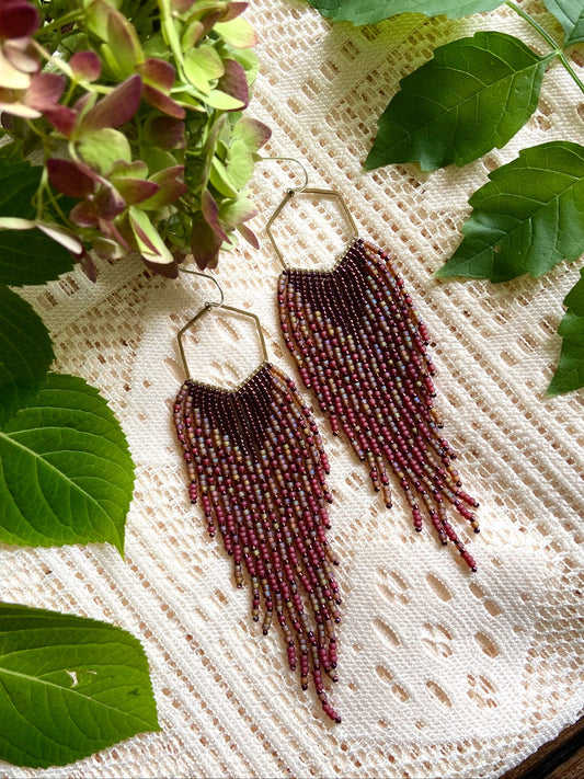 Beaded earrings on a textured surface with green leaves around