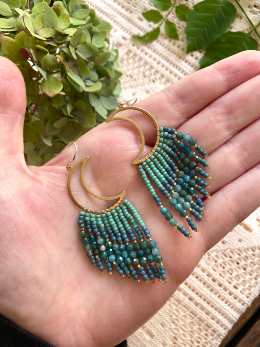 Turquoise beaded earrings on a hand with a natural background